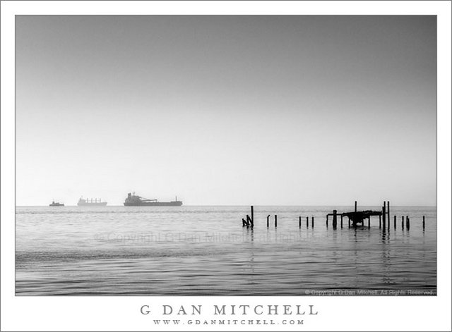 Three Ships at Anchor, San Francisco Bay - Black and white photograph of three ships anchored beyond old dock pilings in luminous morning light on San Francisco Bay