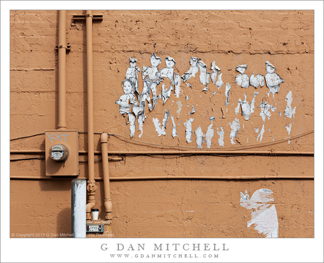 Brown Wall with Pipes and Worn Paper Figures, Fremont District - Worn paper figures glued to a brown wall with pipes and conduit, Fremont District, Seattle Washington