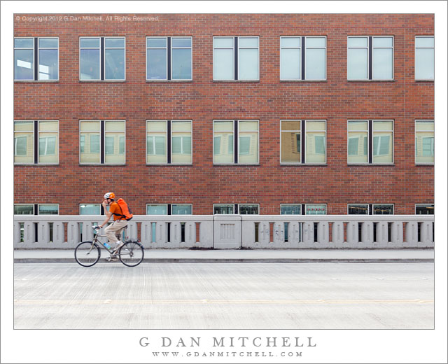 Bicycle Rider, Brick Wall - A bicycle rider in orange rides past a brick wall, Seattle, Washington